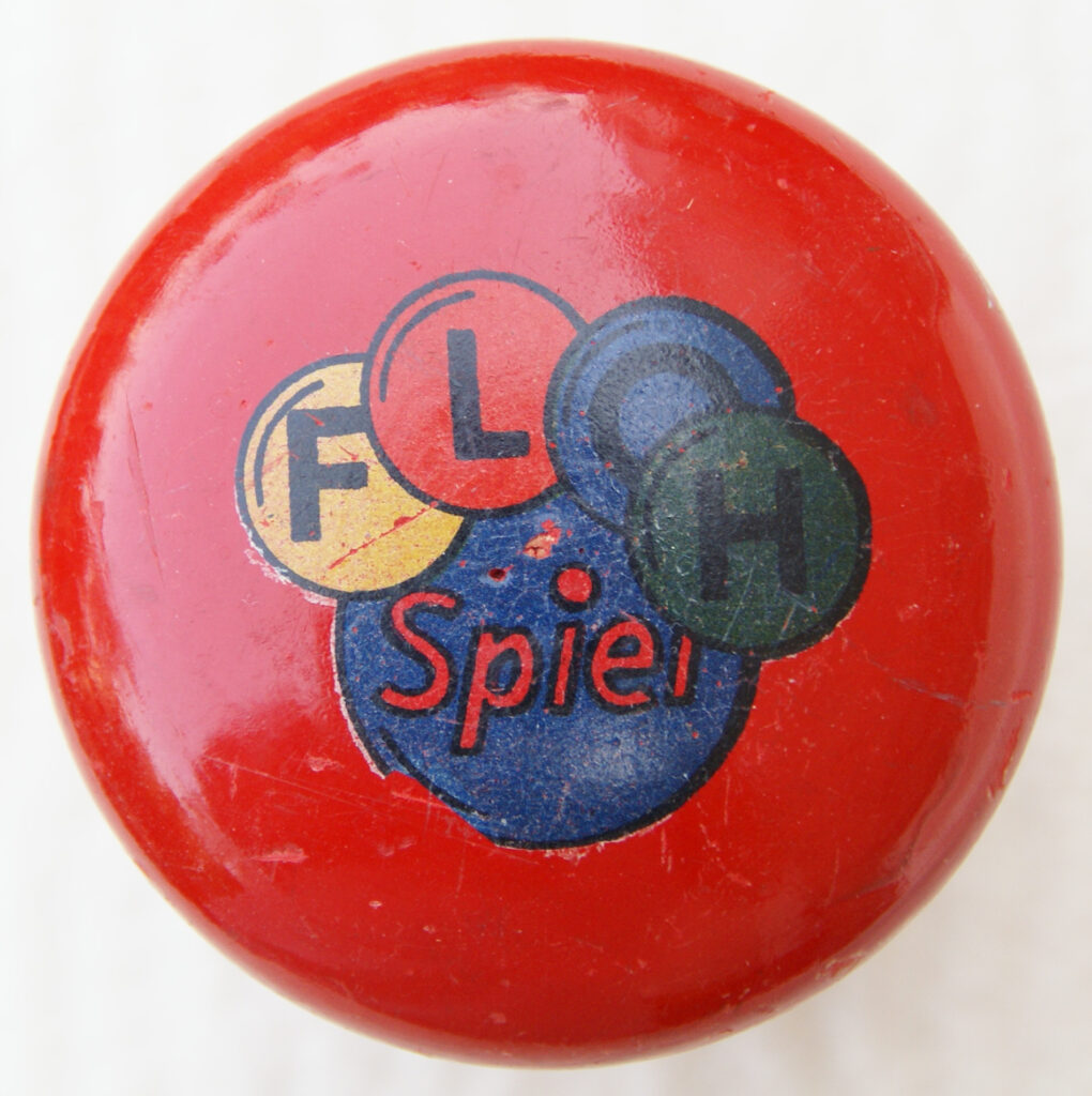Tucker Tw ID • UNK-101c1 — AGPI ID • G-30820c1 — publisher • (unknown, German) — title • FLOH Spiel — notes • Red wooden mushroom container. Letters of "FLOH" on different colored winks.