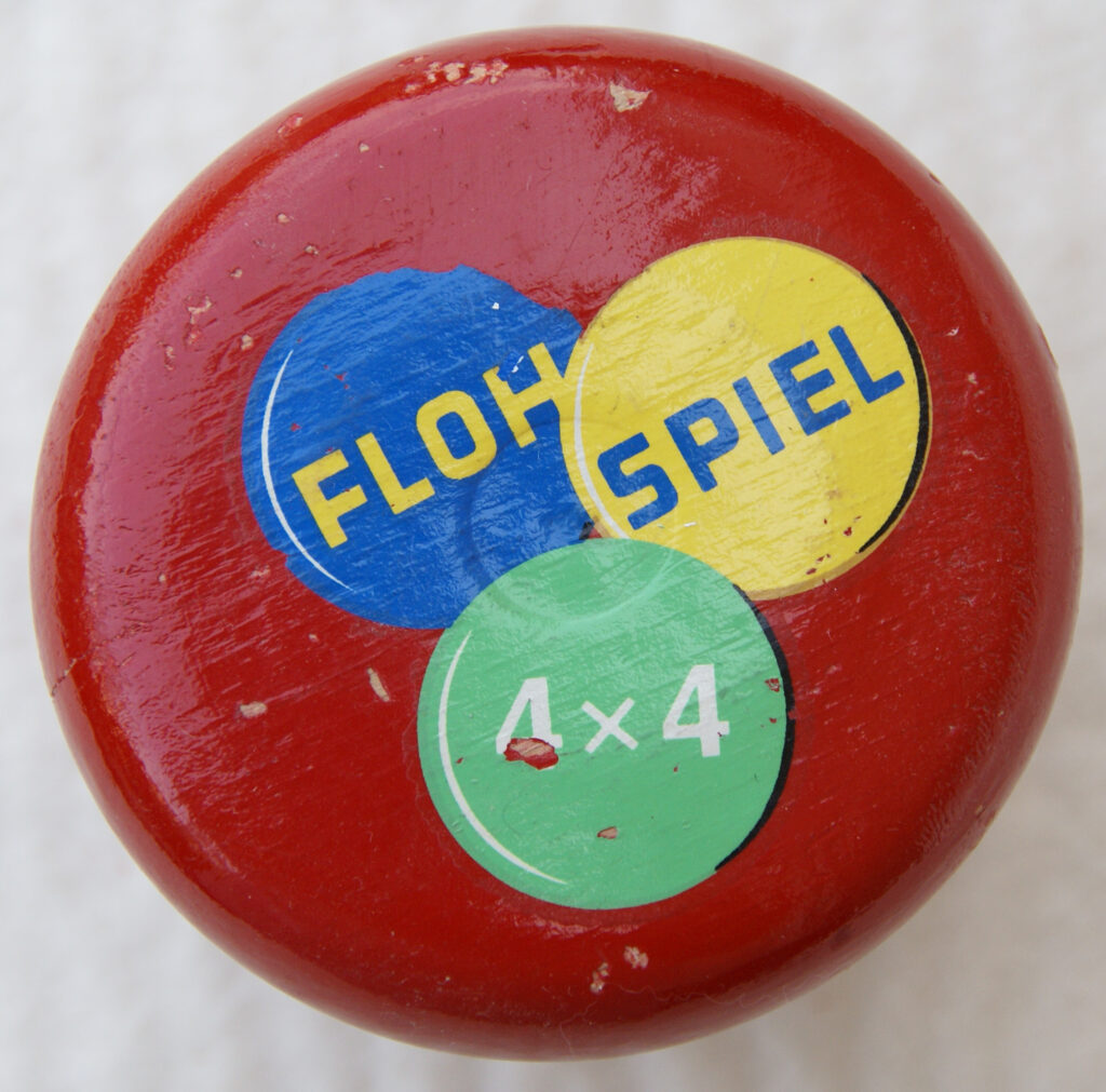 Tucker Tw ID • UNK-167c1 — AGPI ID • G-38355c1 — publisher • (unknown, German) — title • FLOH SPIEL 4x4 — notes • Red wooden mushroom container. "FLOH" on blue wink, "SPIEL" on yellow wink, "4x4" on green wink.